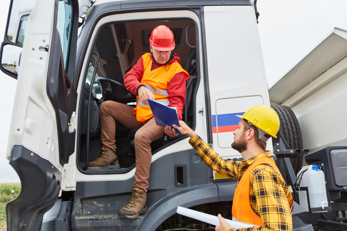 CDL Truck driver brings delivery to construction site with worker