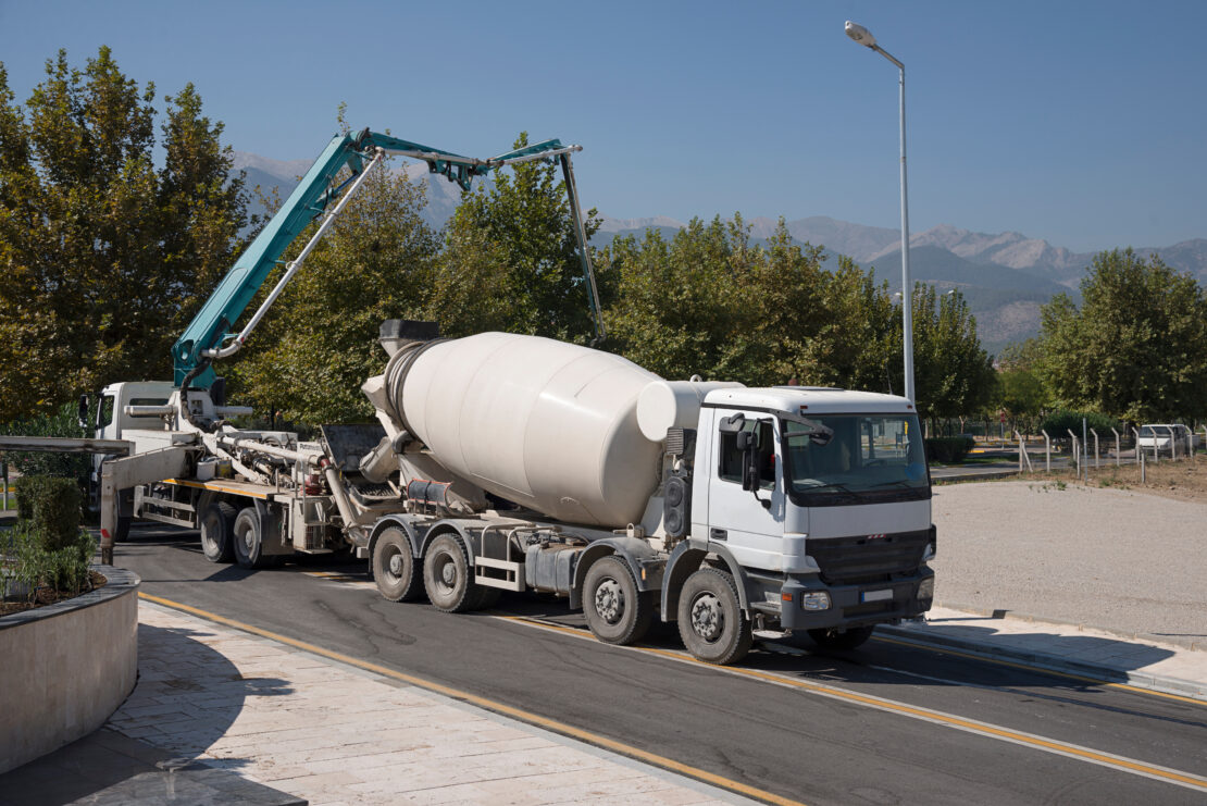 A concrete mixer truck is parked on an access road right in front of a crane