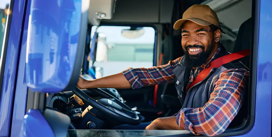 Happy black truck driver behind steering wheel in cabin looking at camera.