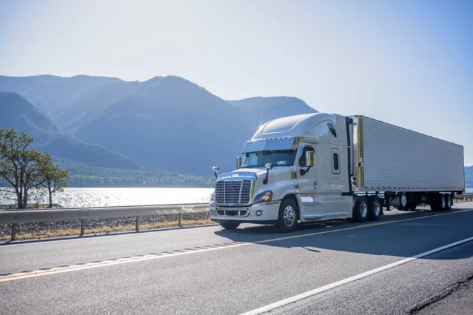 Semi truck on the road with a river and mountains in the background
