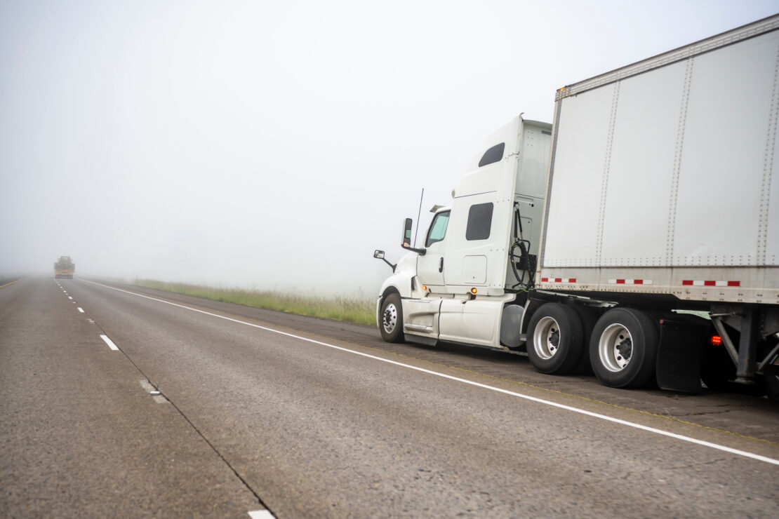 A semi-truck pulled over on a highway shoulder during a foggy day